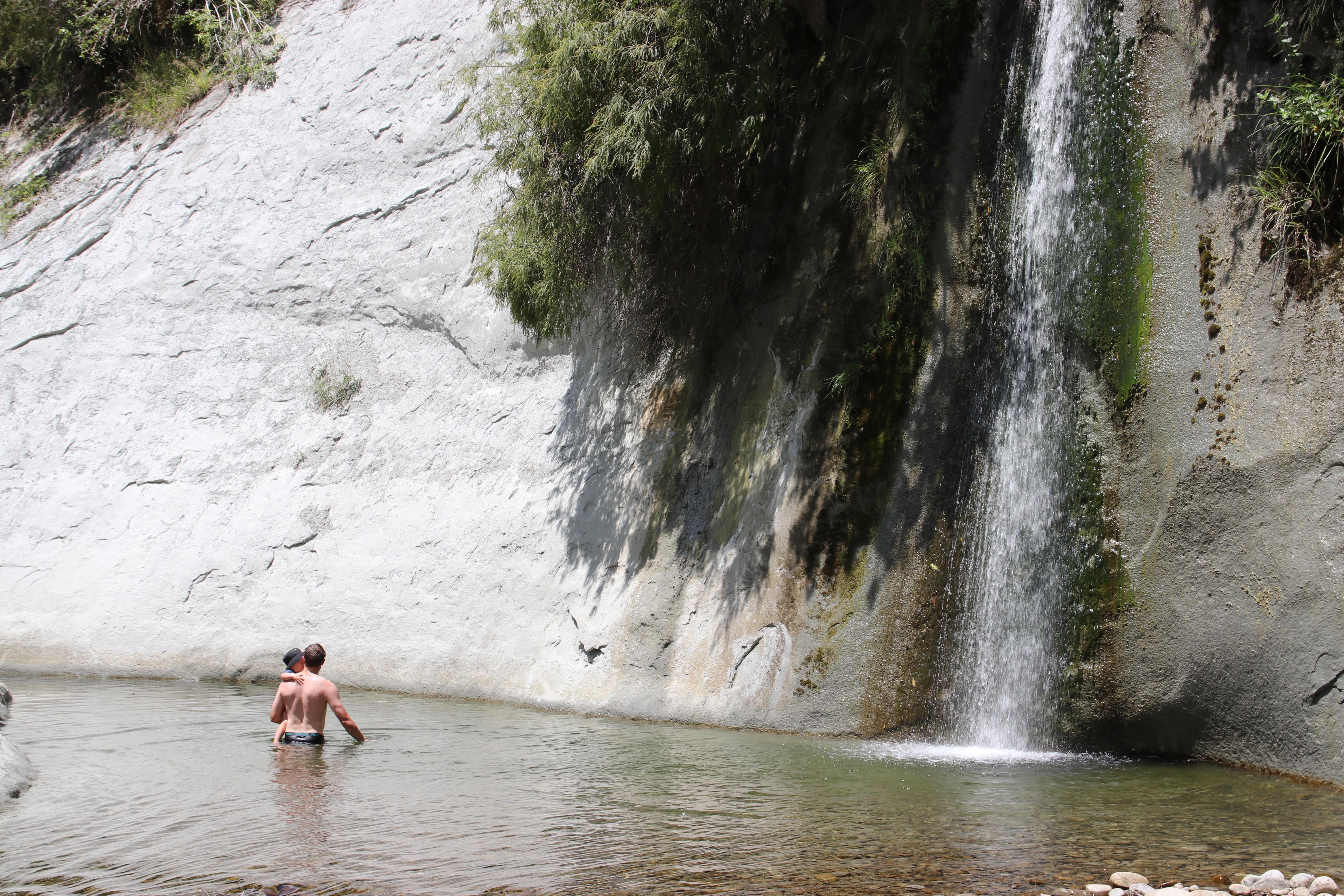 Father and son swimming near a waterfall